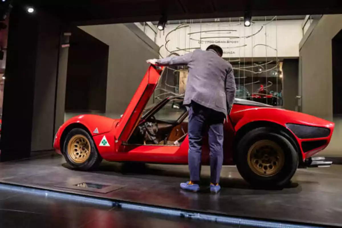 Un hombre observa el interior de un automóvil deportivo rojo con la puerta abierta en una exhibición.