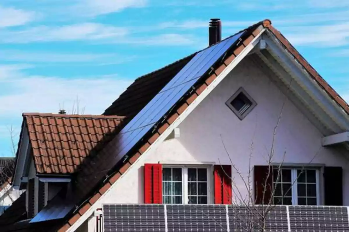 Casa con paneles solares en el techo bajo un cielo azul.
