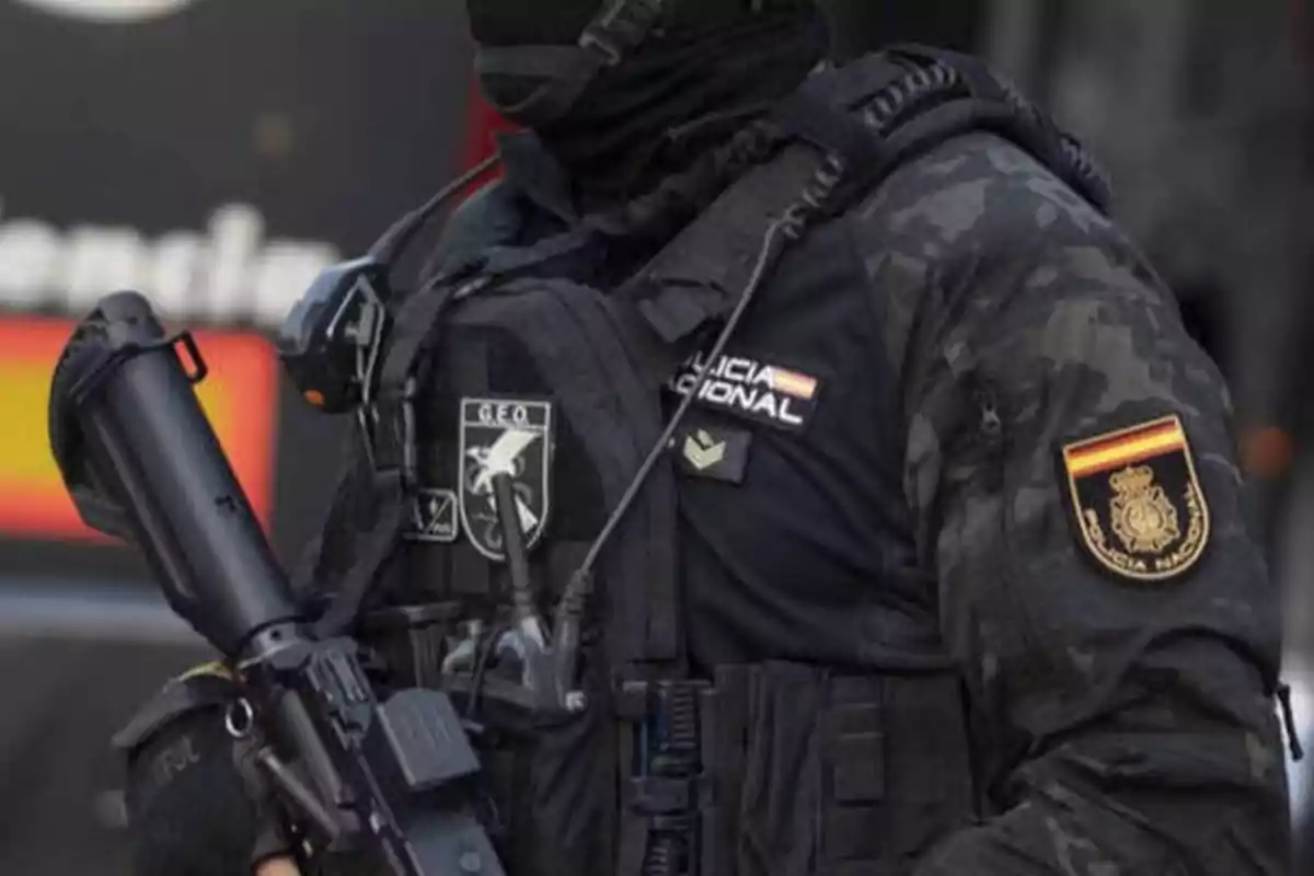 Un agente de la Policía Nacional de España vestido con uniforme táctico y equipo de protección, sosteniendo un arma.