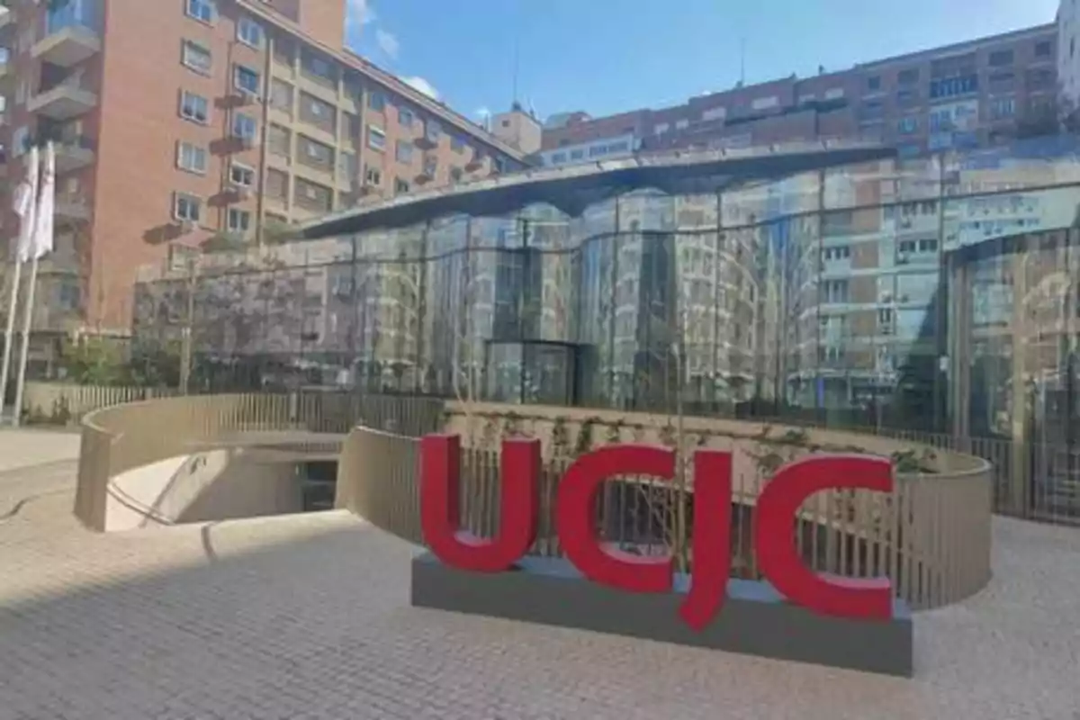 Edificio moderno con fachada de vidrio y un letrero grande de UCJC en la entrada.