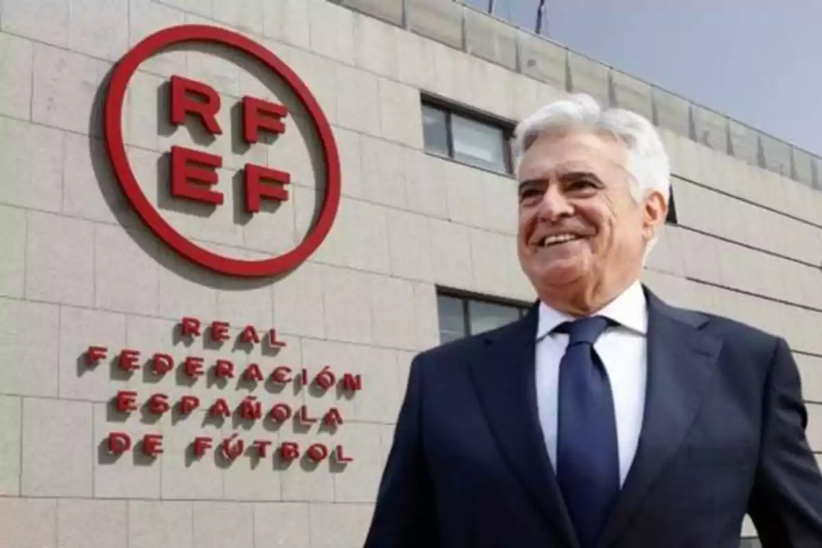 Hombre de traje frente al edificio de la Real Federación Española de Fútbol con el logotipo de la RFEF en la pared.