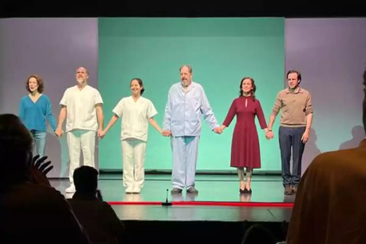 Un grupo de actores en el escenario tomados de la mano durante una reverencia al final de una obra de teatro.