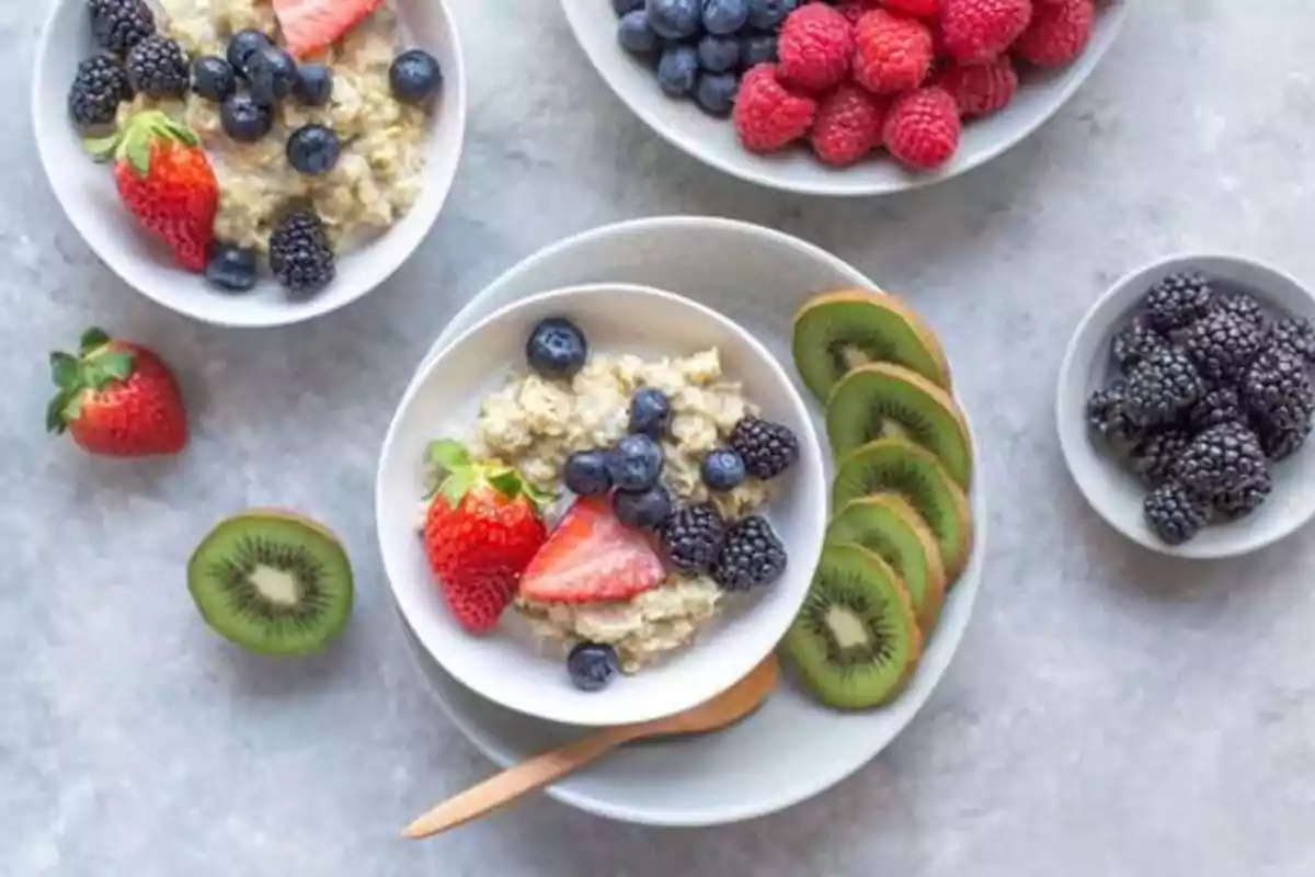 Un desayuno saludable con avena, fresas, moras, arándanos y kiwi en platos sobre una mesa de mármol.