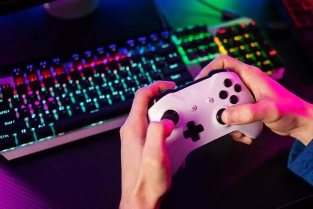 Persona sosteniendo un control de videojuegos frente a un teclado retroiluminado.