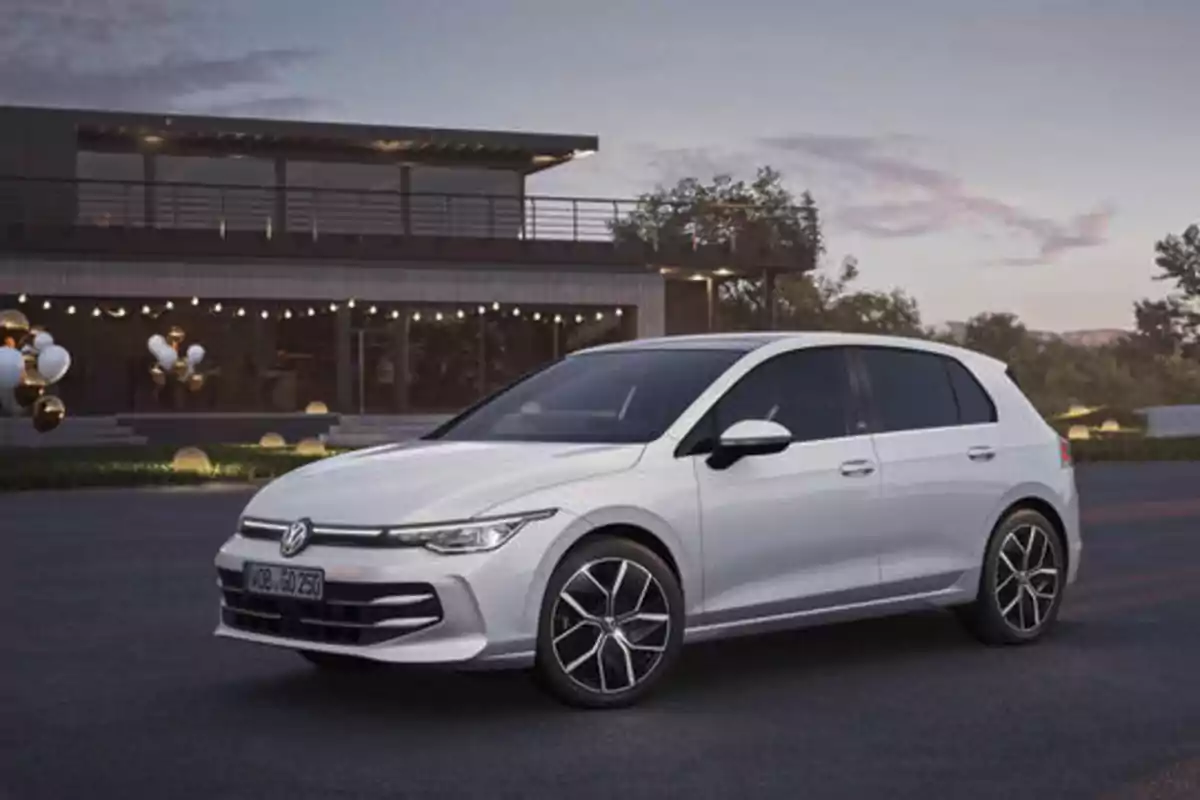 Un coche Volkswagen blanco estacionado frente a una casa moderna al atardecer.