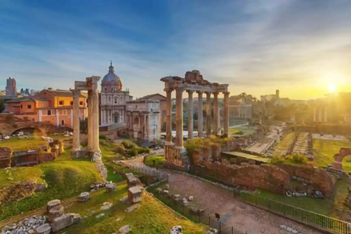 Ruinas del Foro Romano en Roma al atardecer con columnas antiguas y edificios históricos bajo un cielo despejado.