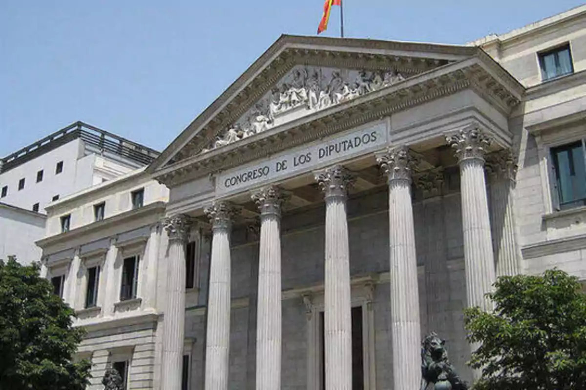 Fachada del Congreso de los Diputados en Madrid, España, con columnas y una bandera española ondeando en la parte superior.