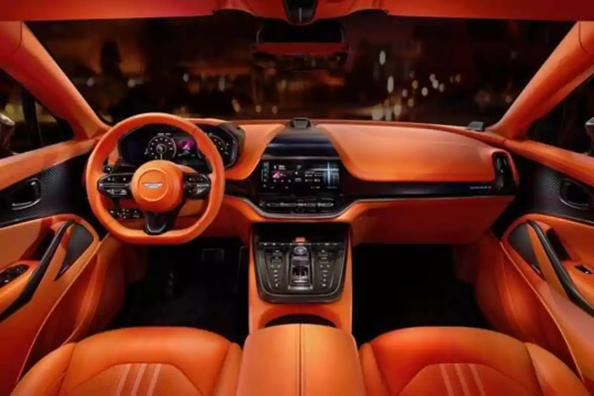 Interior de un automóvil deportivo con asientos y volante de color naranja, tablero moderno y pantalla táctil central.