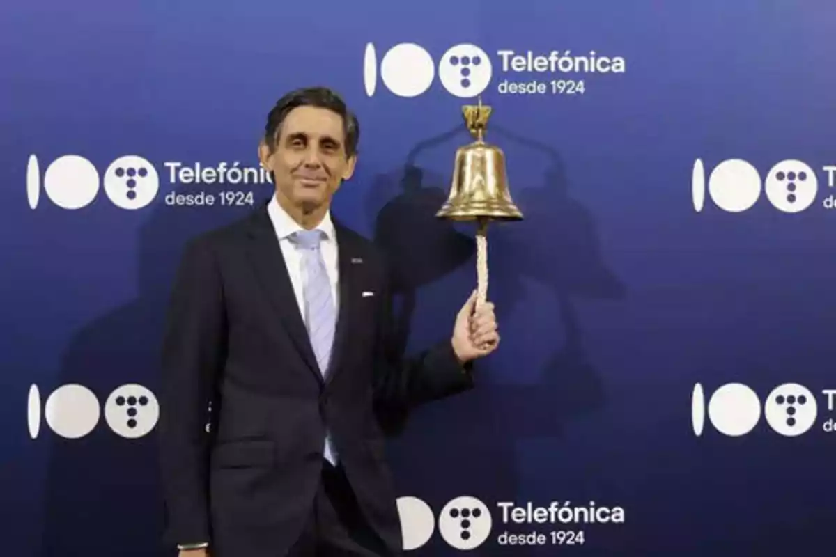 Hombre en traje sosteniendo una campana frente a un fondo azul con el logotipo de Telefónica y el texto "Telefónica desde 1924".