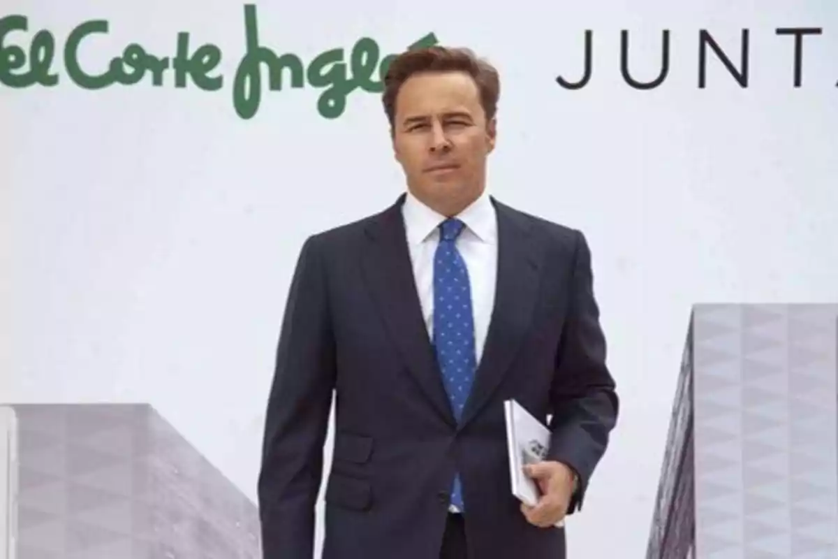 Un hombre de traje y corbata azul con puntos blancos sostiene un documento frente a un fondo con el logotipo de El Corte Inglés y la palabra "JUNTA".