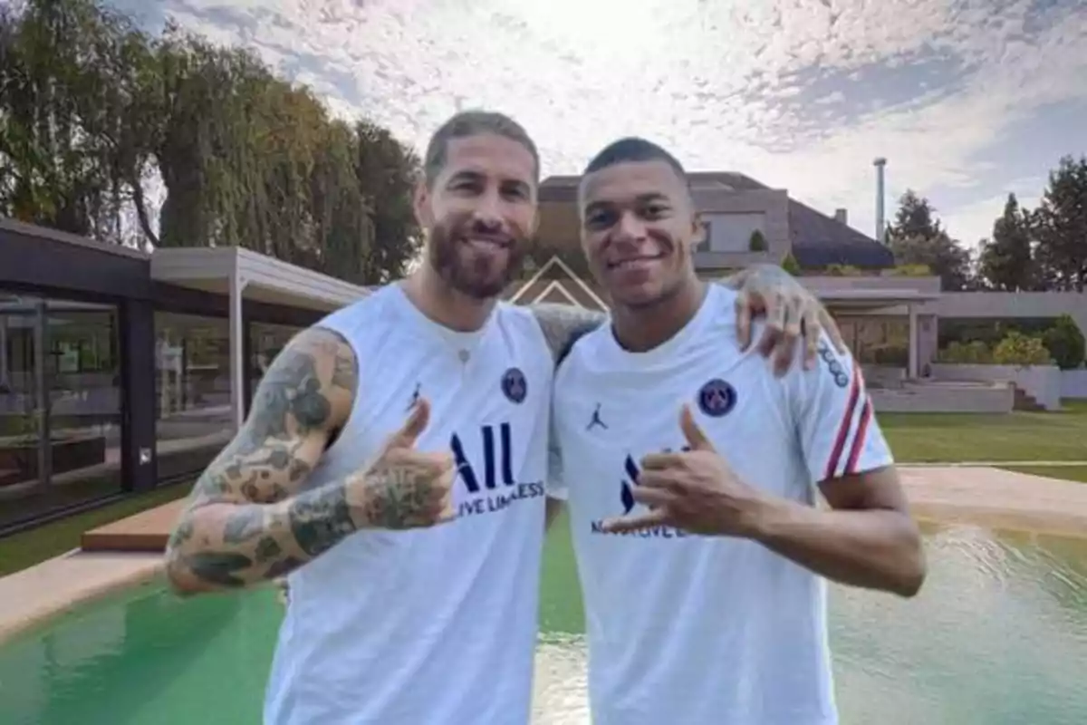 Dos hombres con camisetas del PSG posan juntos sonriendo y haciendo el gesto de pulgar arriba frente a una piscina y una casa moderna.