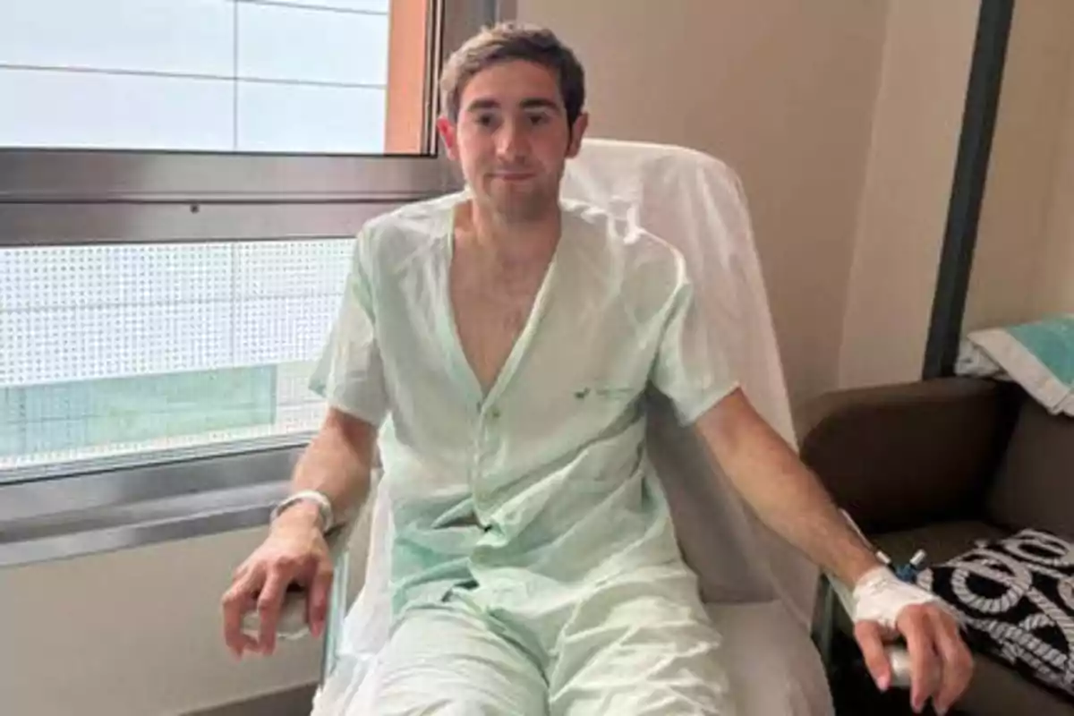 Hombre sentado en una silla de hospital con bata médica y una vía intravenosa en el brazo.