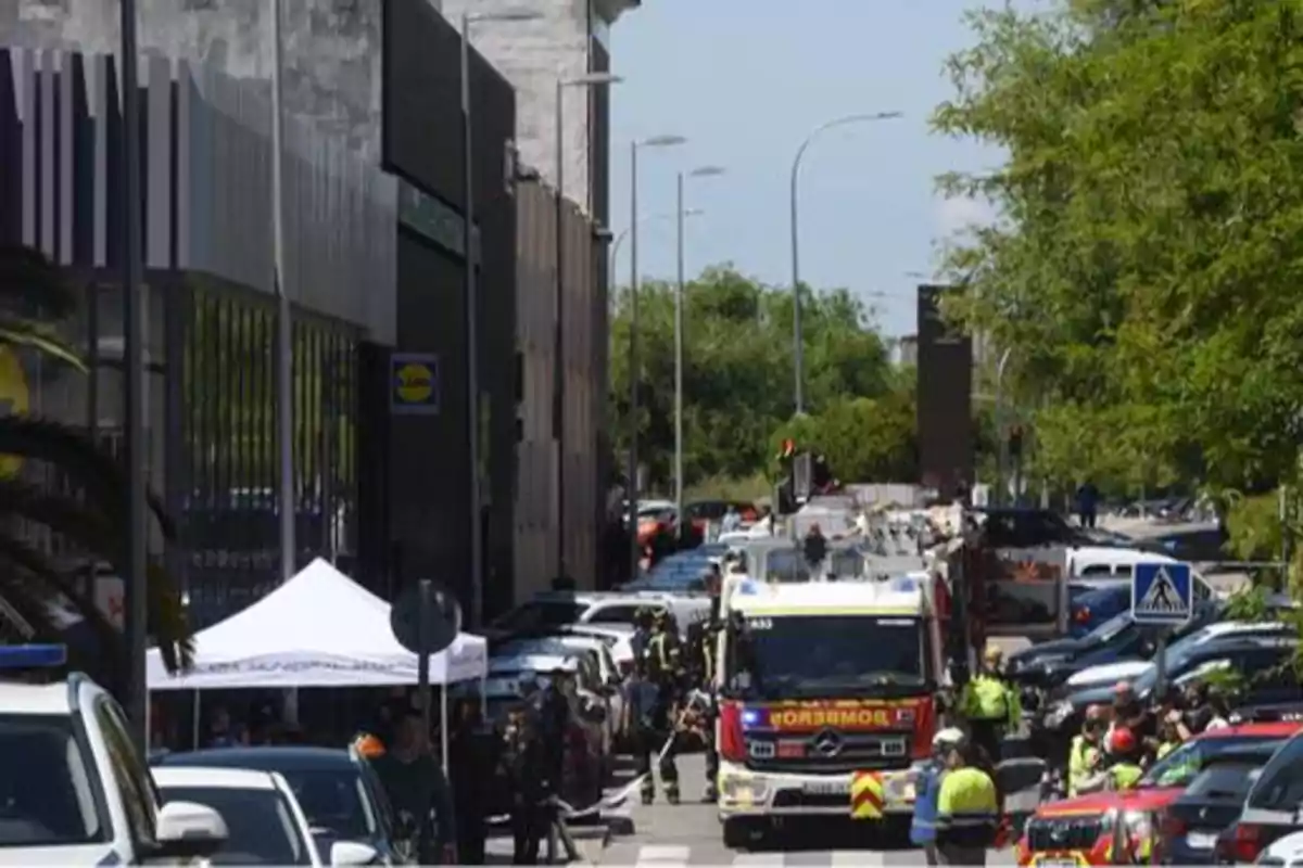 La imagen muestra una calle con varios vehículos de emergencia, incluyendo camiones de bomberos y coches de policía, mientras los equipos de rescate trabajan en la escena.
