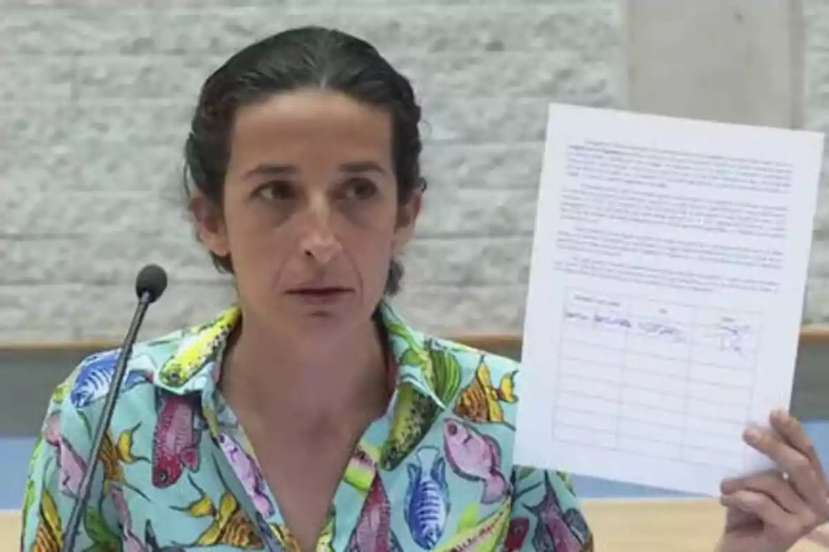 Persona con camisa colorida sosteniendo un documento mientras habla frente a un micrófono.
