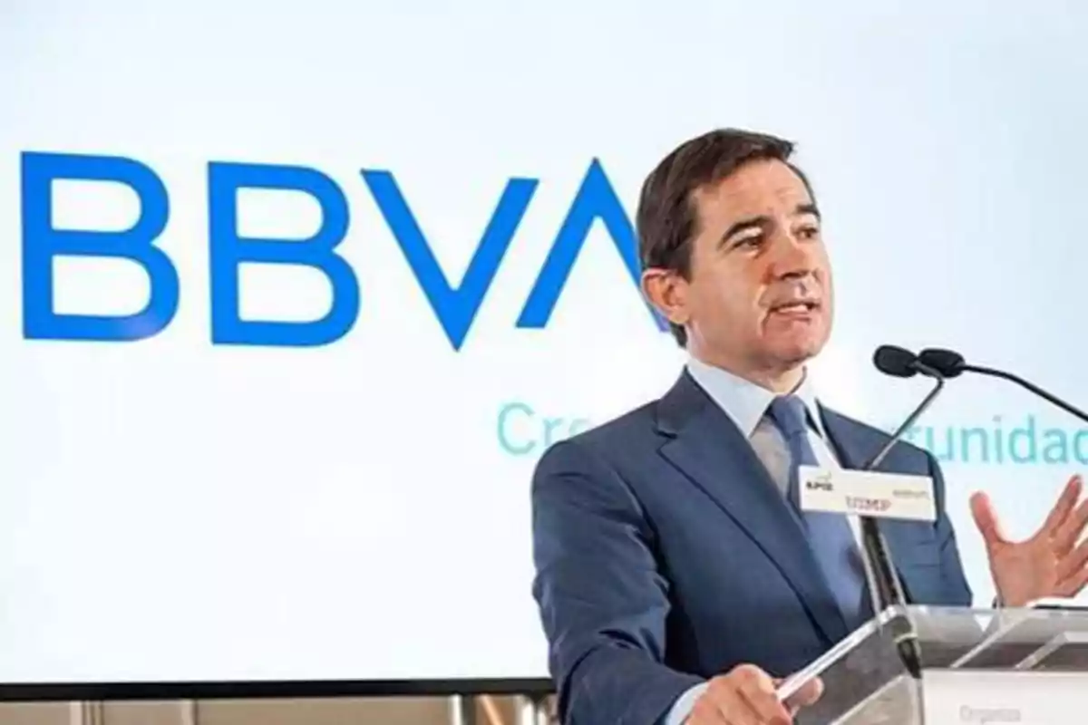 Hombre en traje dando un discurso en un podio con el logotipo de BBVA en el fondo.