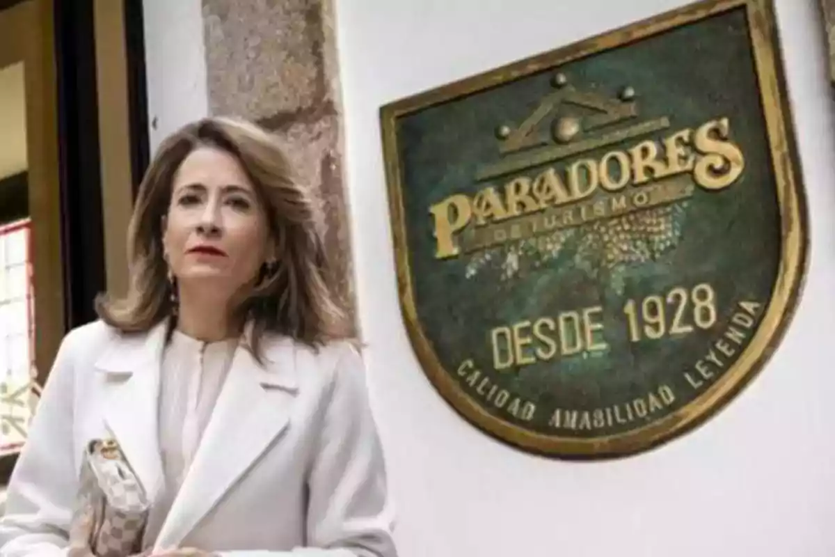 Una mujer con abrigo blanco está de pie junto a un letrero de Paradores de Turismo que indica "Desde 1928".