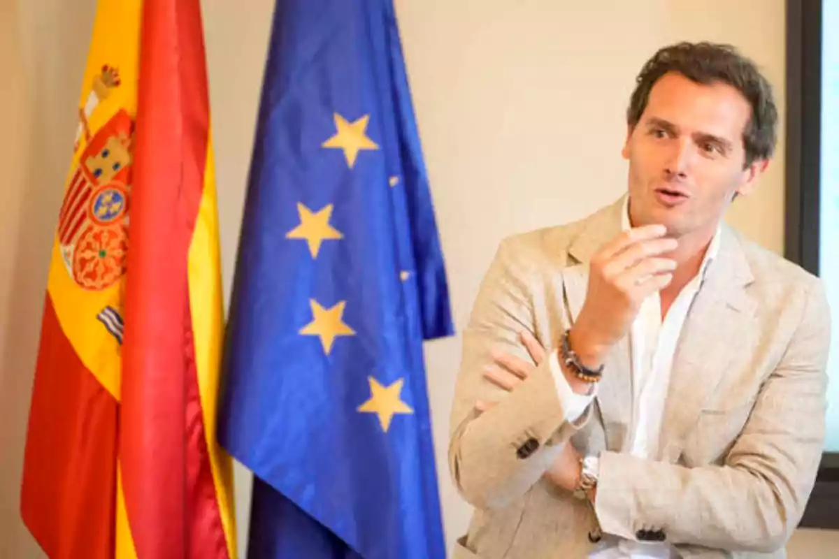 Un hombre hablando gesticulando con las banderas de España y la Unión Europea detrás de él.