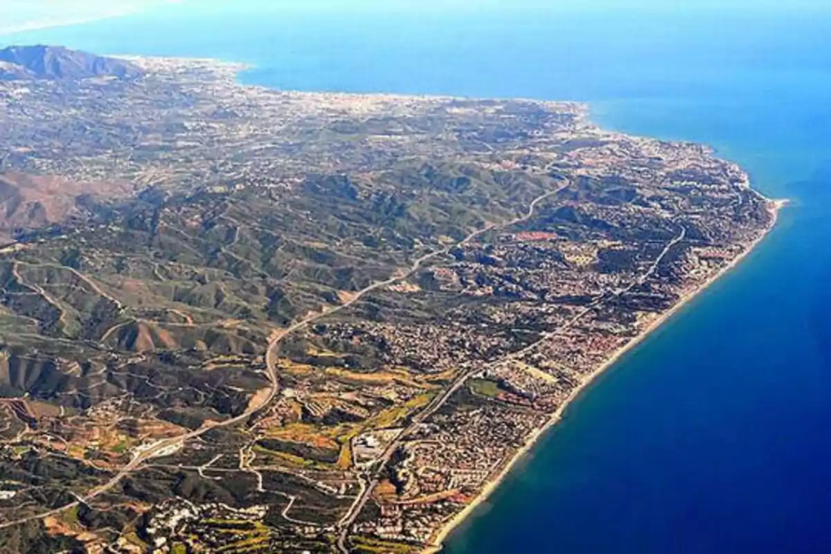 Vista aérea de una costa con montañas y áreas urbanas junto al mar.