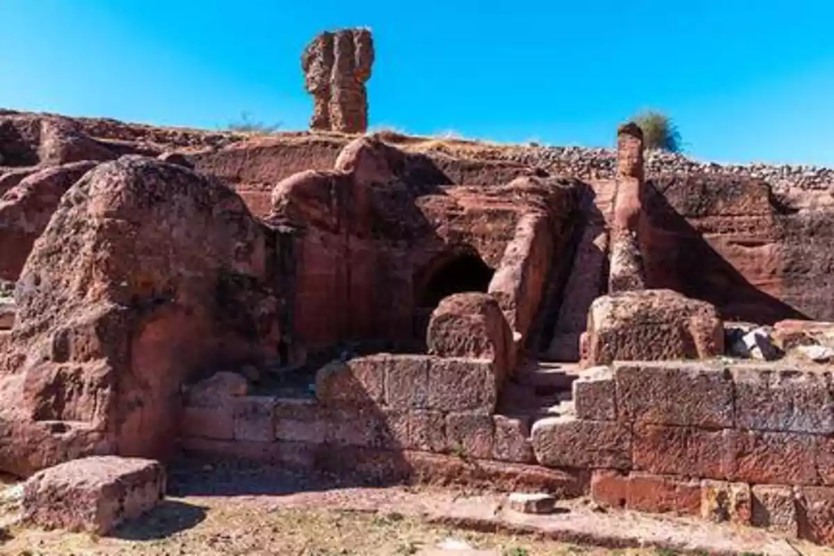 Ruinas de una estructura antigua tallada en roca roja bajo un cielo despejado.