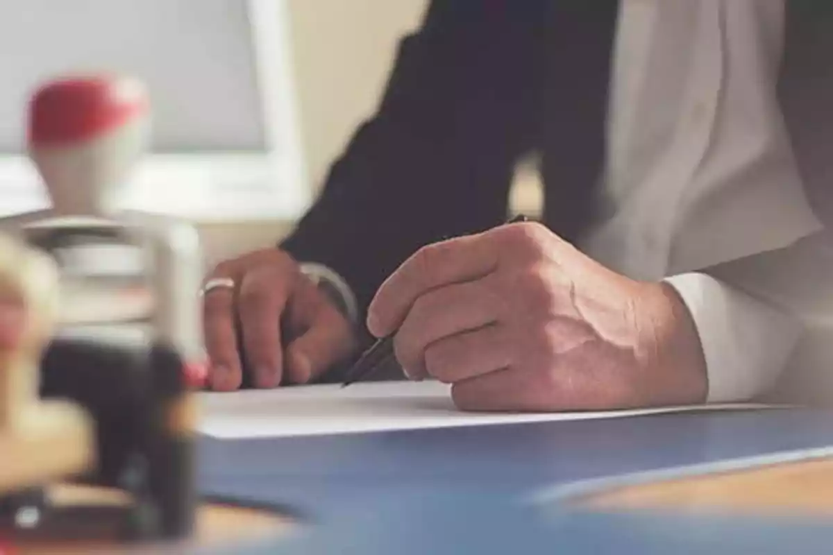 Persona escribiendo en un escritorio con un bolígrafo.