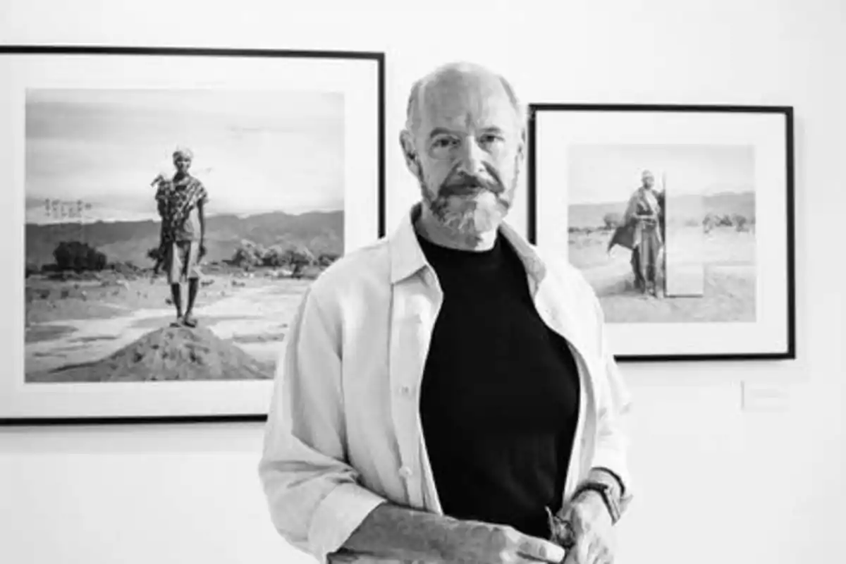 Un hombre de pie frente a dos fotografías enmarcadas en blanco y negro en una galería de arte.