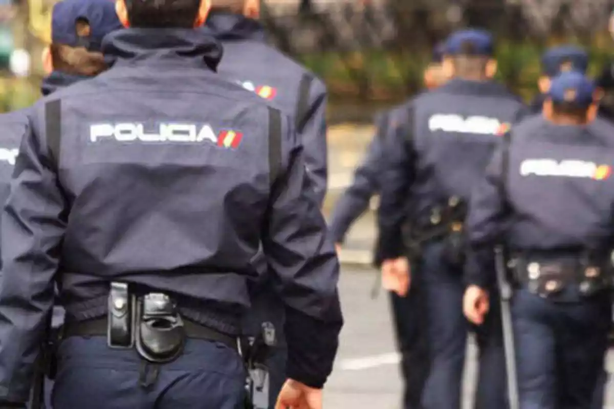 Policías caminando en fila con uniformes azules y la palabra "POLICÍA" en la espalda.