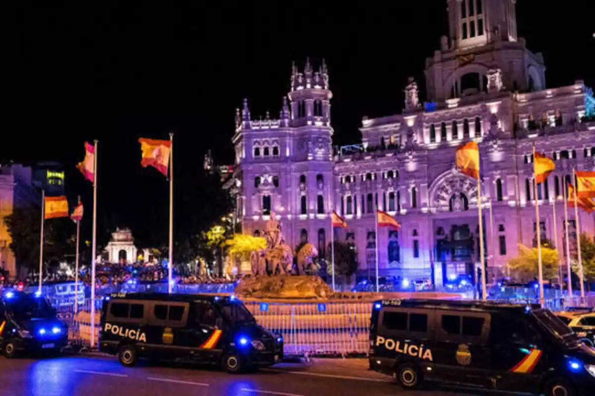 Edificio iluminado por la noche con banderas y vehículos de policía en primer plano.