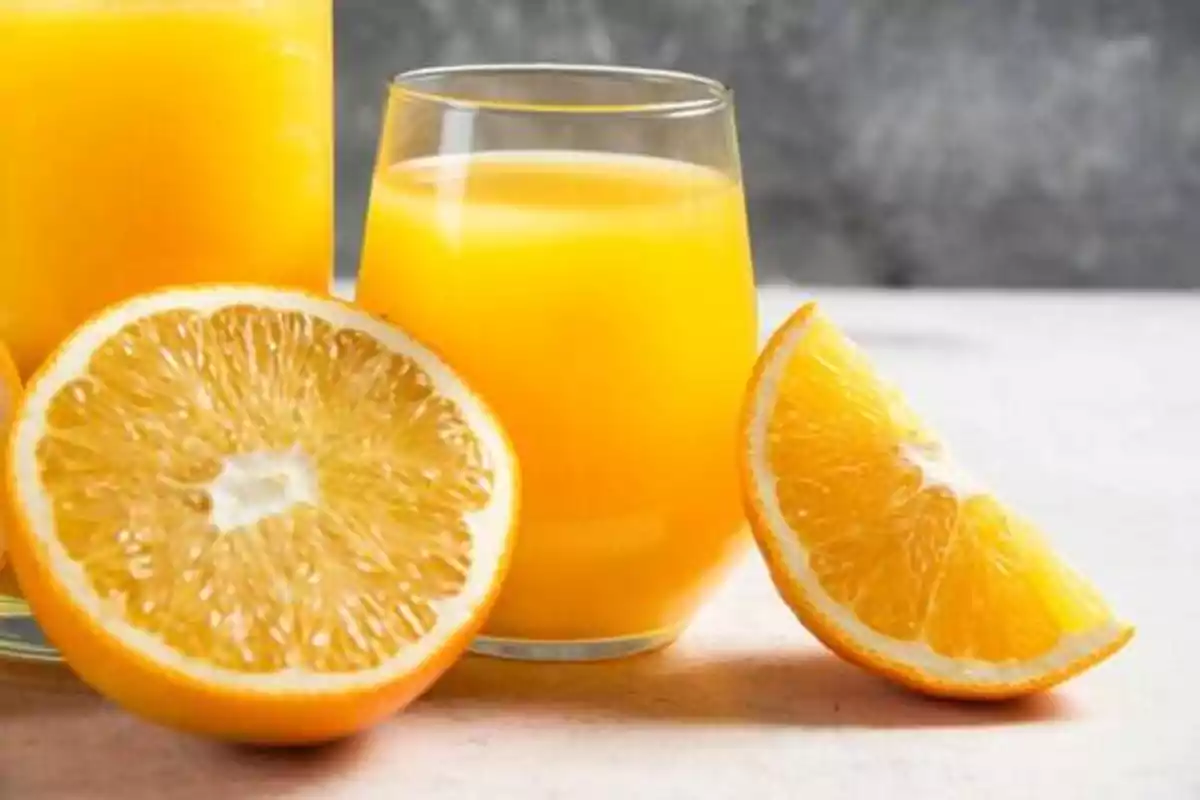 Vaso de jugo de naranja junto a rodajas de naranja fresca.