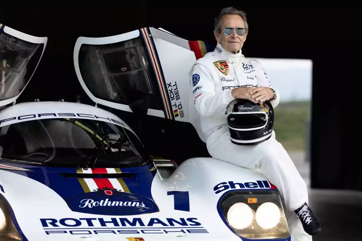 Jacky Ickx con traje de carreras y gafas de sol está sentado sobre un auto de carreras Porsche con el logo de Rothmans.