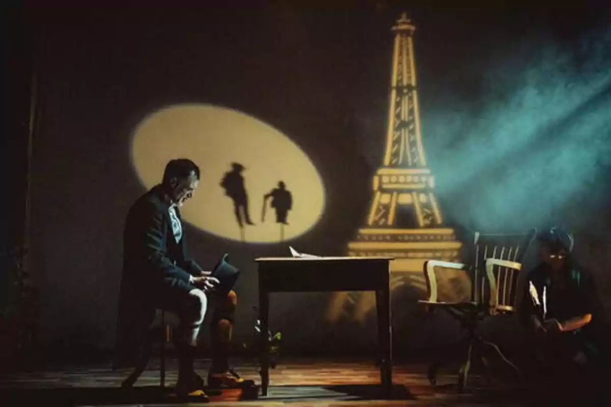 Un hombre sentado en una silla frente a una mesa, con una figura de la Torre Eiffel y sombras de dos personas proyectadas en la pared detrás de él.