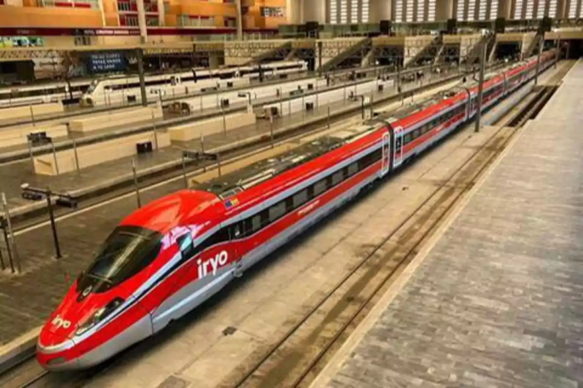 Un tren de alta velocidad rojo y plateado de la compañía Iryo estacionado en una plataforma de una estación de tren moderna.