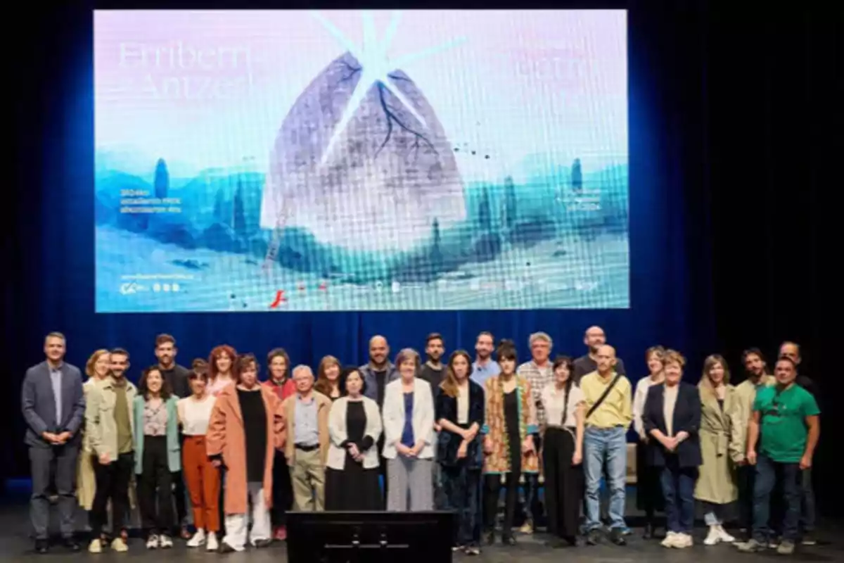 Un grupo de personas posando en un escenario frente a una pantalla grande que muestra un cartel con el texto "Erriberri Antzerki".