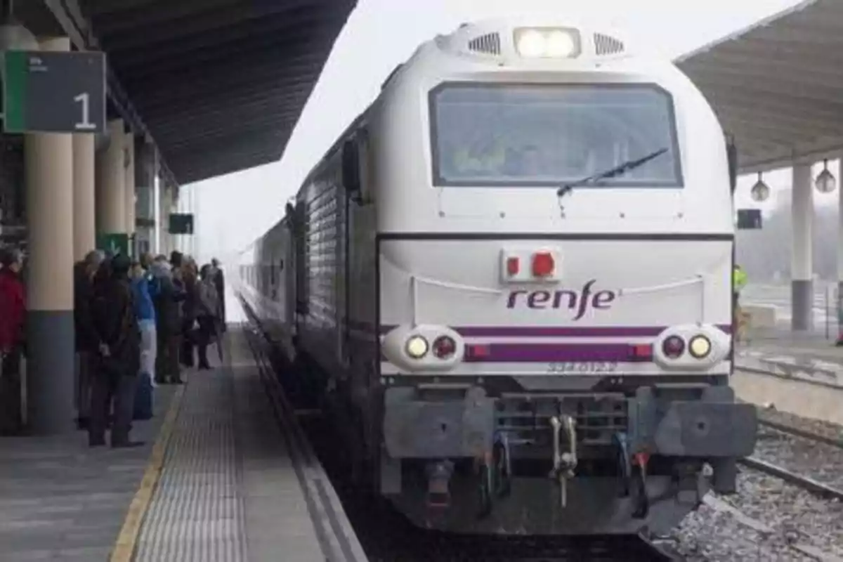 Un tren de la compañía Renfe en una estación con personas esperando en el andén.