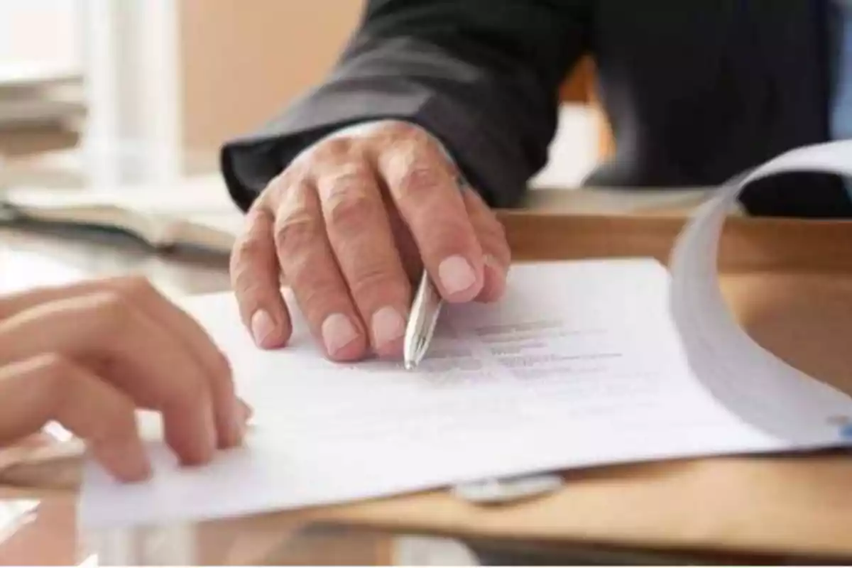 Manos de personas revisando y firmando documentos en una oficina.