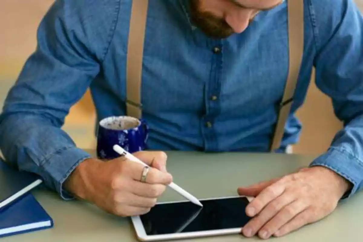 Hombre usando un lápiz digital en una tableta mientras sostiene una taza de café.