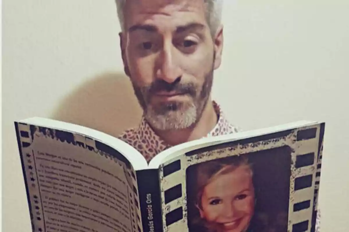 Hombre con barba y cabello canoso leyendo un libro con la imagen de una mujer en la portada.