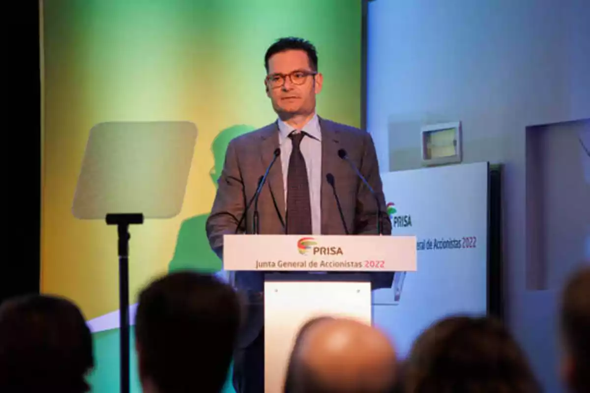 Hombre de traje y gafas hablando en un podio durante la Junta General de Accionistas 2022 de PRISA.