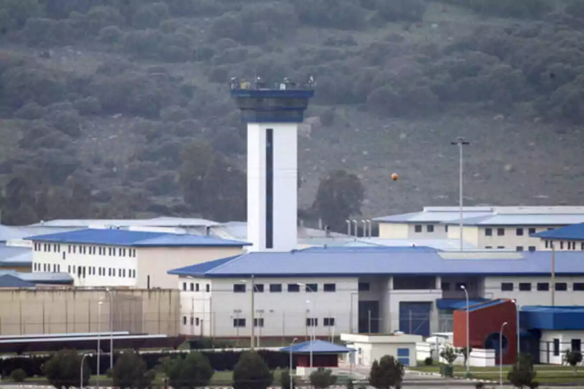 Vista de un complejo penitenciario con edificios de techos azules y una torre de vigilancia en un entorno montañoso.