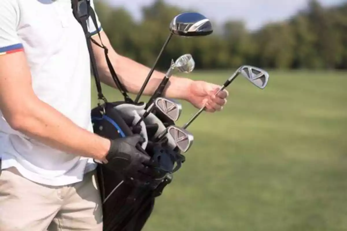 Persona sosteniendo una bolsa de palos de golf en un campo de golf.
