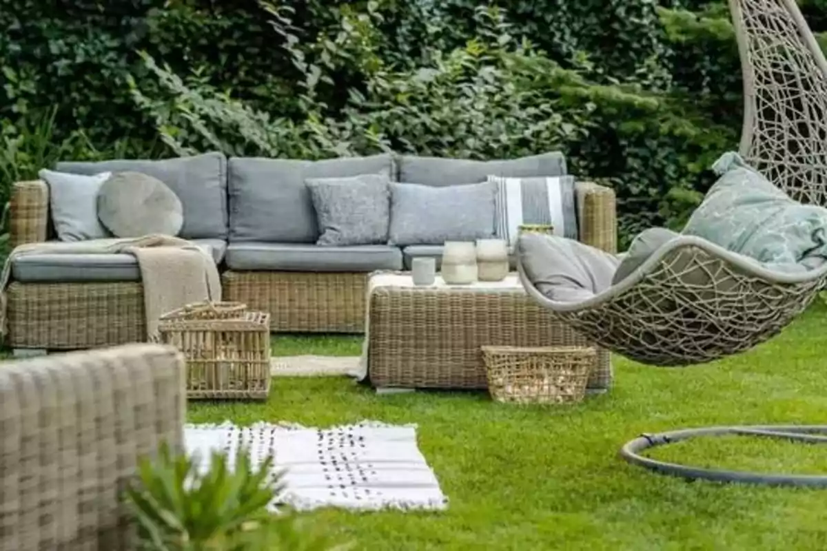 Muebles de jardín con cojines grises y una silla colgante en un entorno verde.