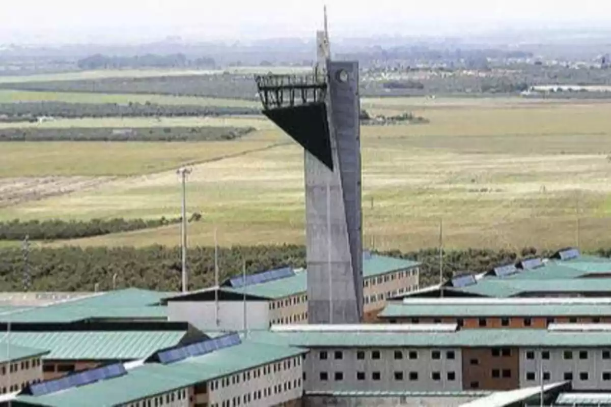 Vista aérea de un complejo penitenciario con una torre de vigilancia en el centro y campos abiertos en el fondo.