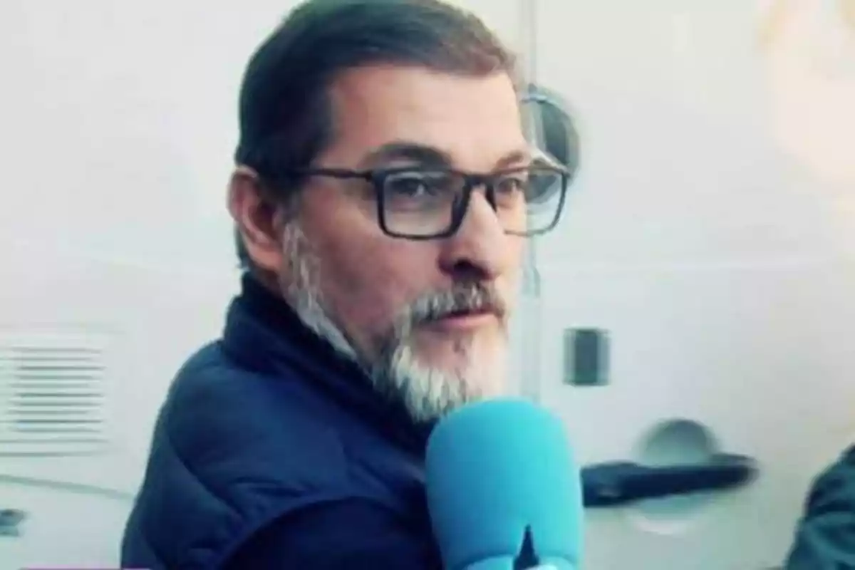 Hombre con barba y gafas siendo entrevistado con un micrófono azul.