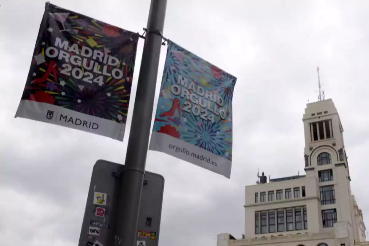 Banderas colgadas en un poste anunciando el evento "Madrid Orgullo 2024" con un edificio de fondo.