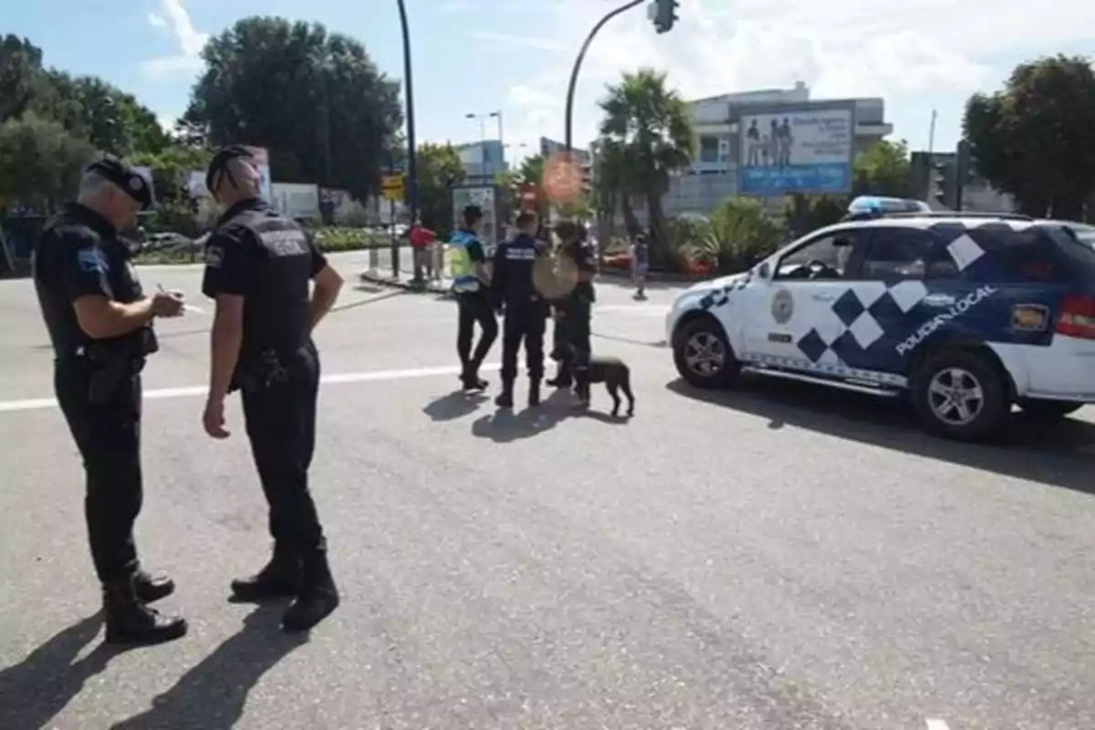 Policías locales con un perro y un coche patrulla en una intersección.