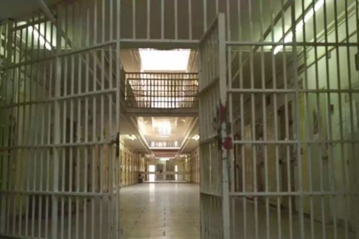 Pasillo de una prisión con puertas de rejas abiertas y celdas a los lados.
