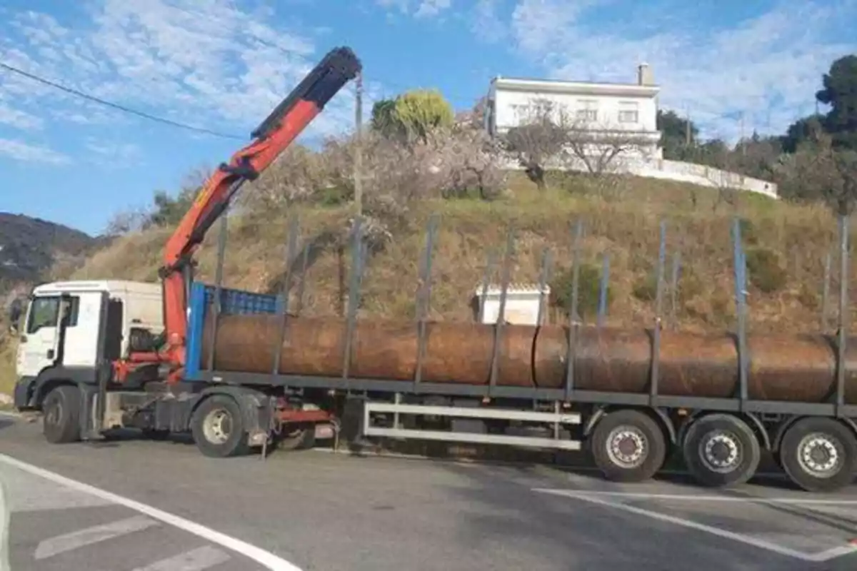 Un camión con una grúa transporta grandes tubos metálicos en una carretera.