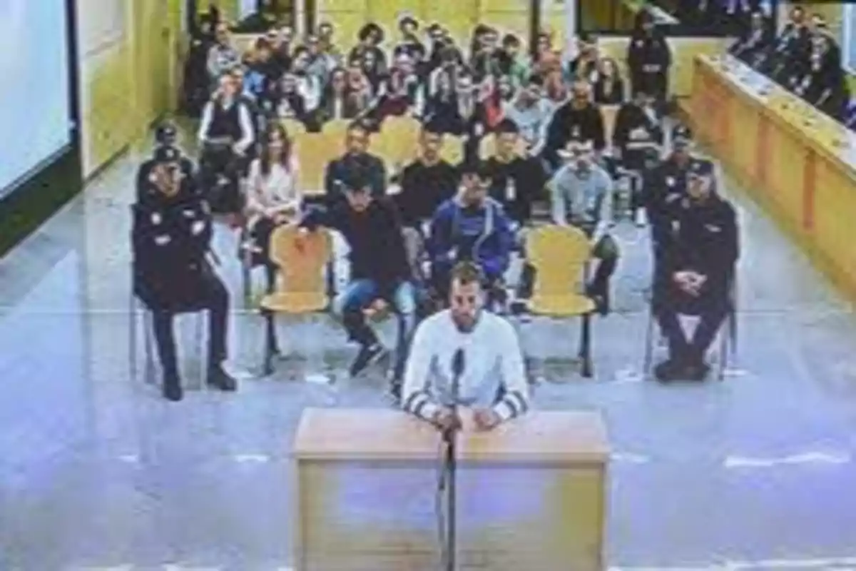 Una persona declarando en un tribunal con público y policías presentes.