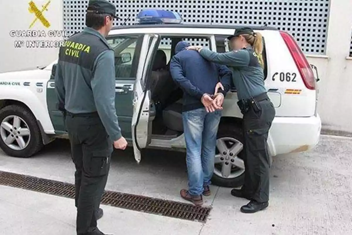 Agentes de la Guardia Civil arrestando a un individuo y colocándolo en la parte trasera de un vehículo oficial.