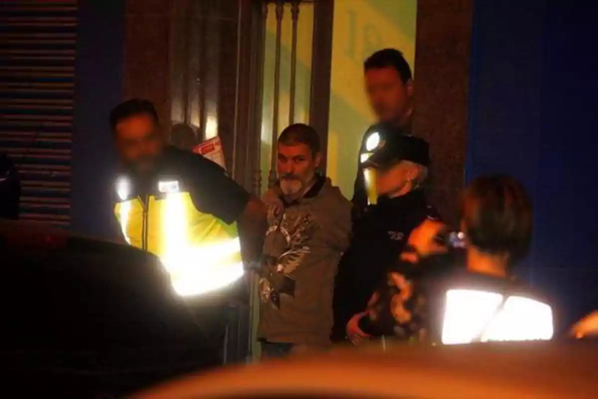 Un hombre esposado es escoltado por varios oficiales de policía en una escena nocturna.