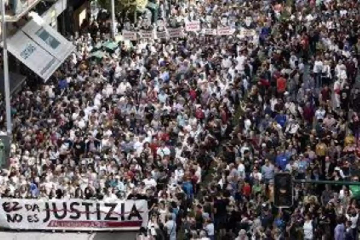 Una multitud de personas participando en una manifestación en una calle, con pancartas y carteles visibles.